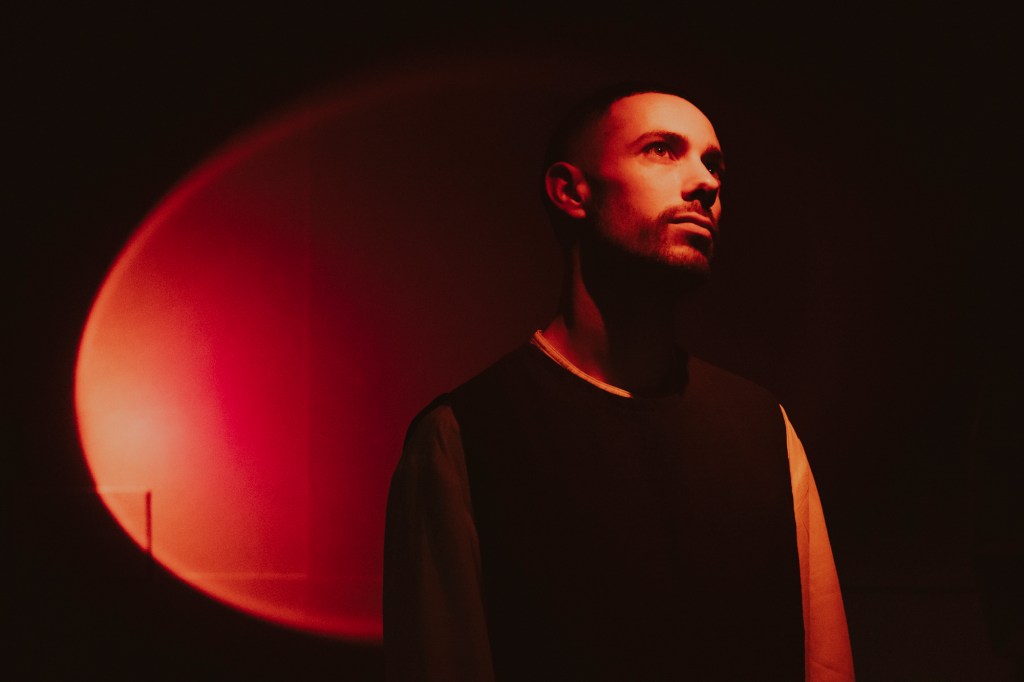 Musician Bofirax posing sideways with his face looking up, with a bright red light illuminating his face and a red backlit background.